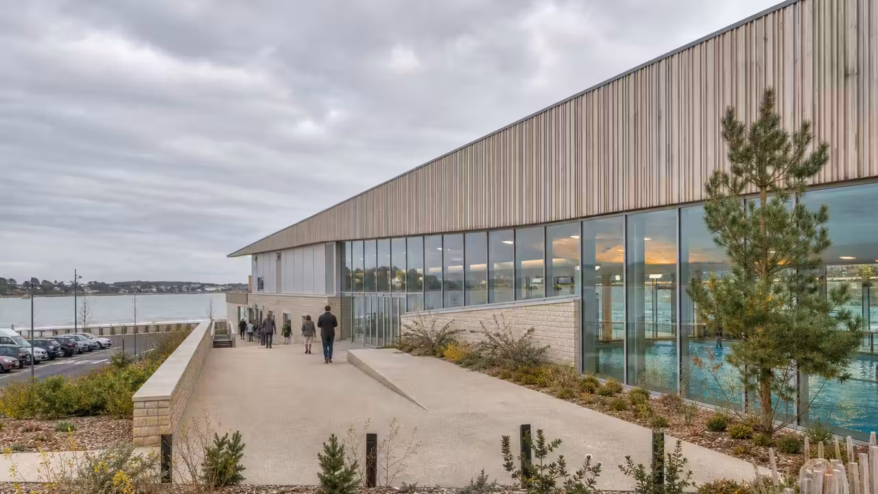 Vue extérieure d’un centre aquatique contemporain avec deux bassins visibles derrière de larges baies vitrées