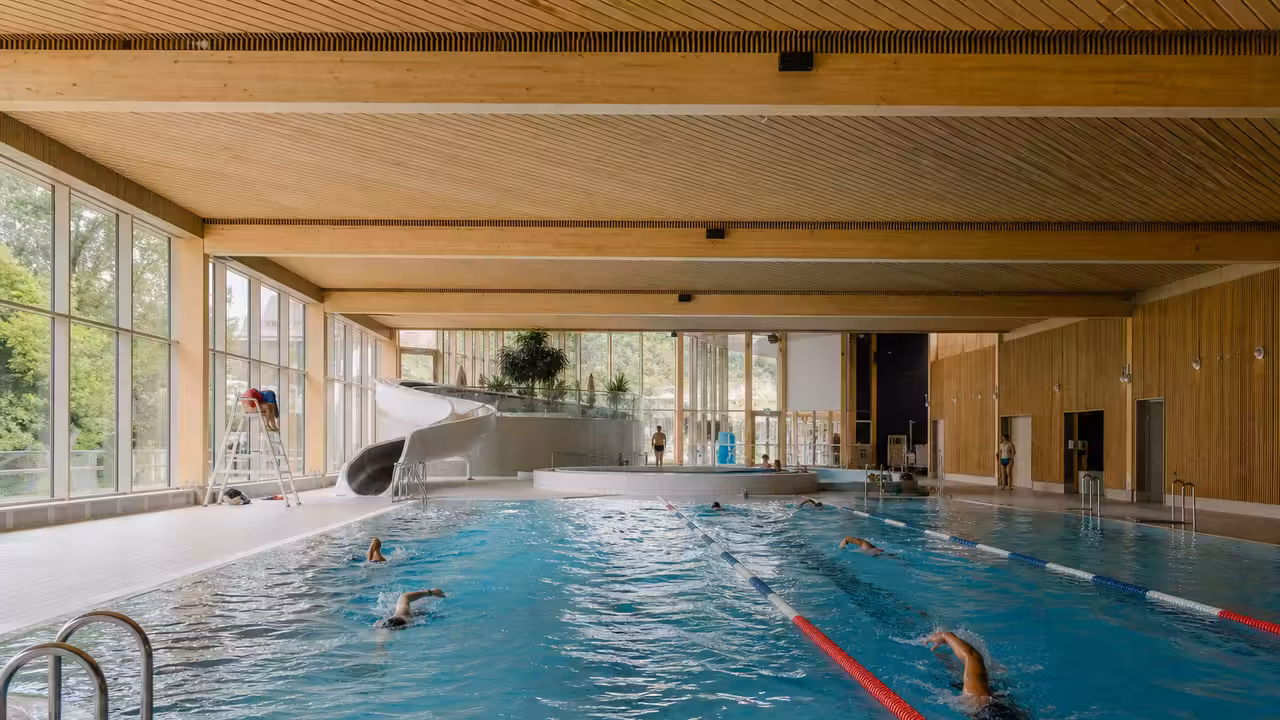 Bassin public rénové avec lignes de nage, espace de détente et grand toboggan sous lumière naturelle