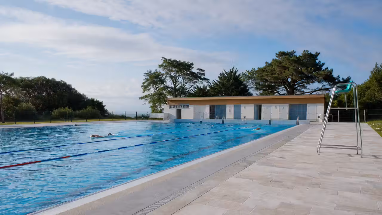 Bassin extérieur municipal avec lignes de nage, plages minérales et végétation sous un soleil d’été