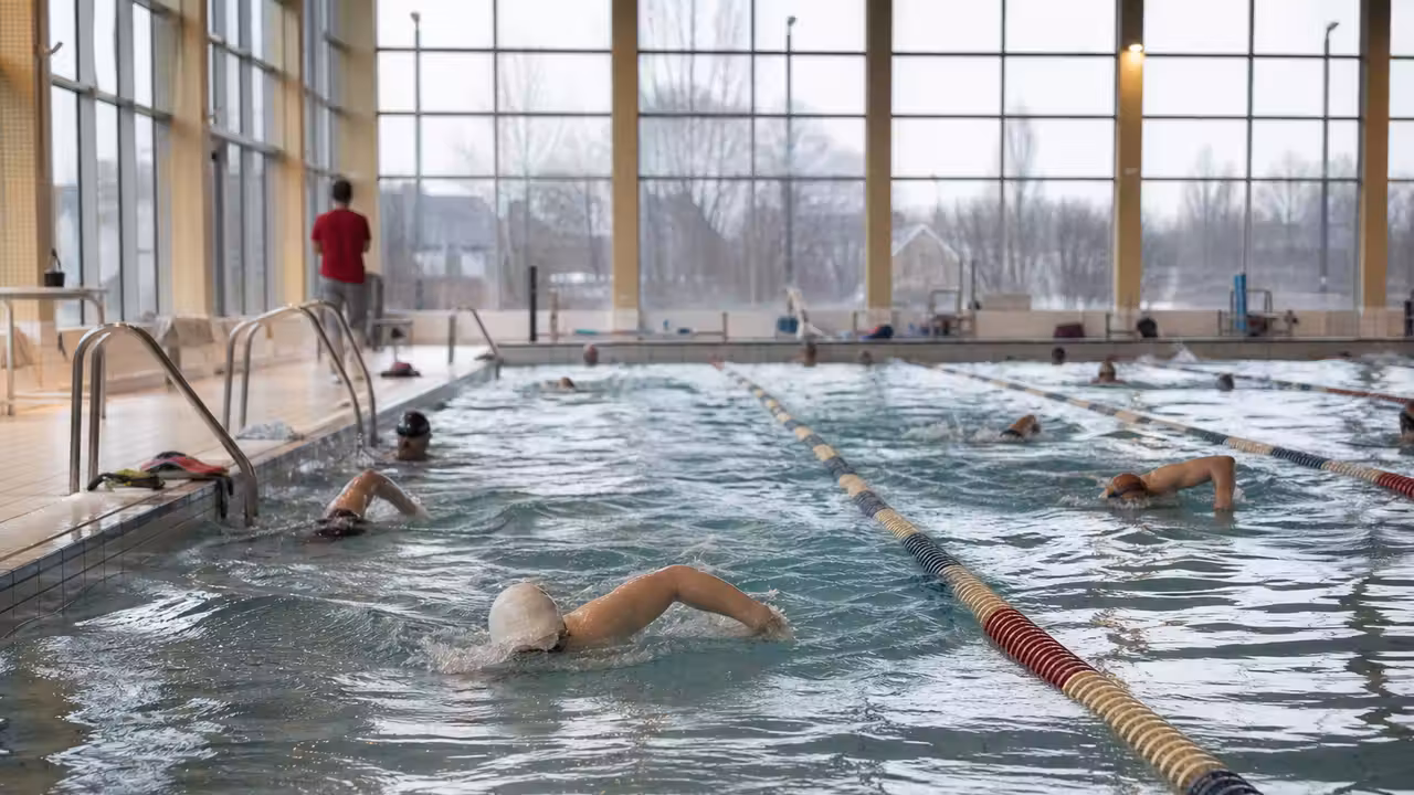 Nageurs répartis dans les lignes d’un bassin couvert très fréquenté, vus depuis le bord de la piscine