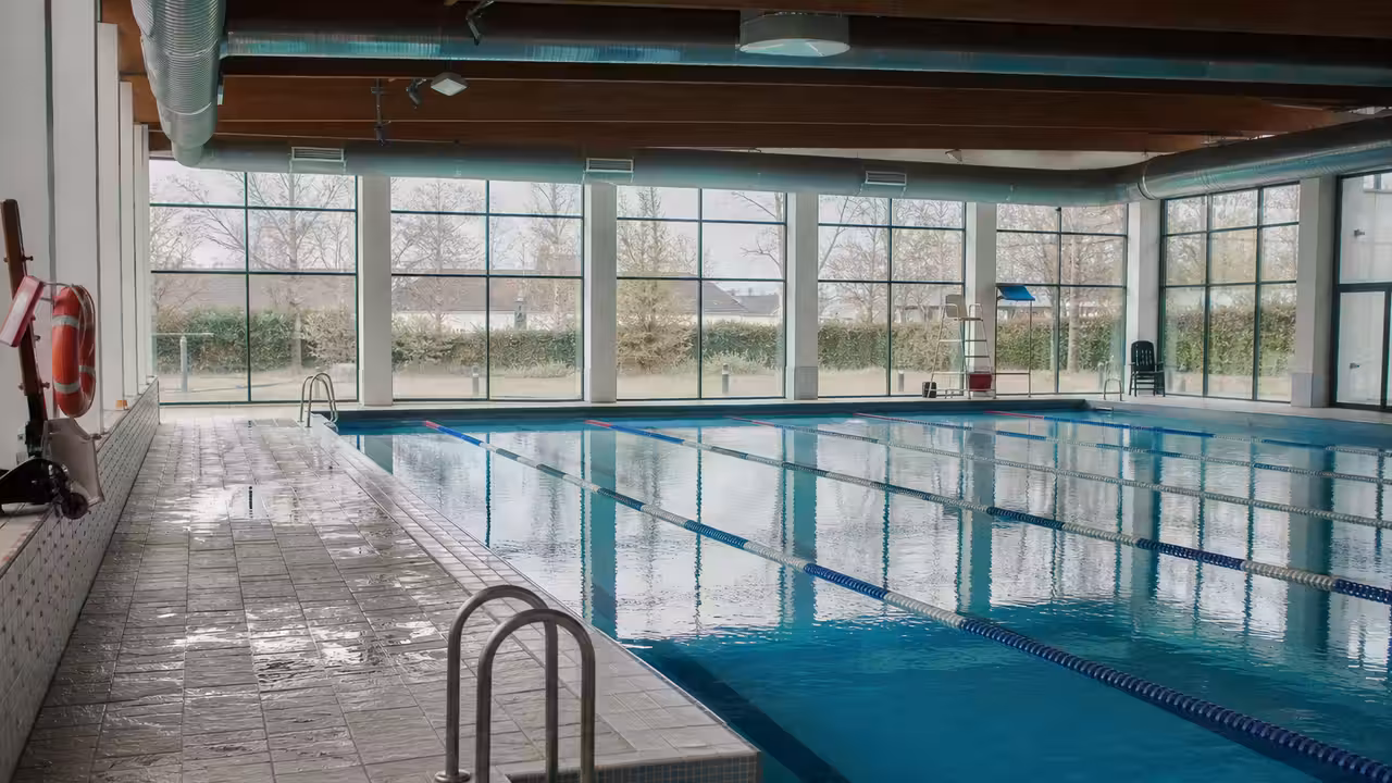 Bassin couvert vide avec lignes d’eau, larges baies vitrées et système de ventilation au plafond