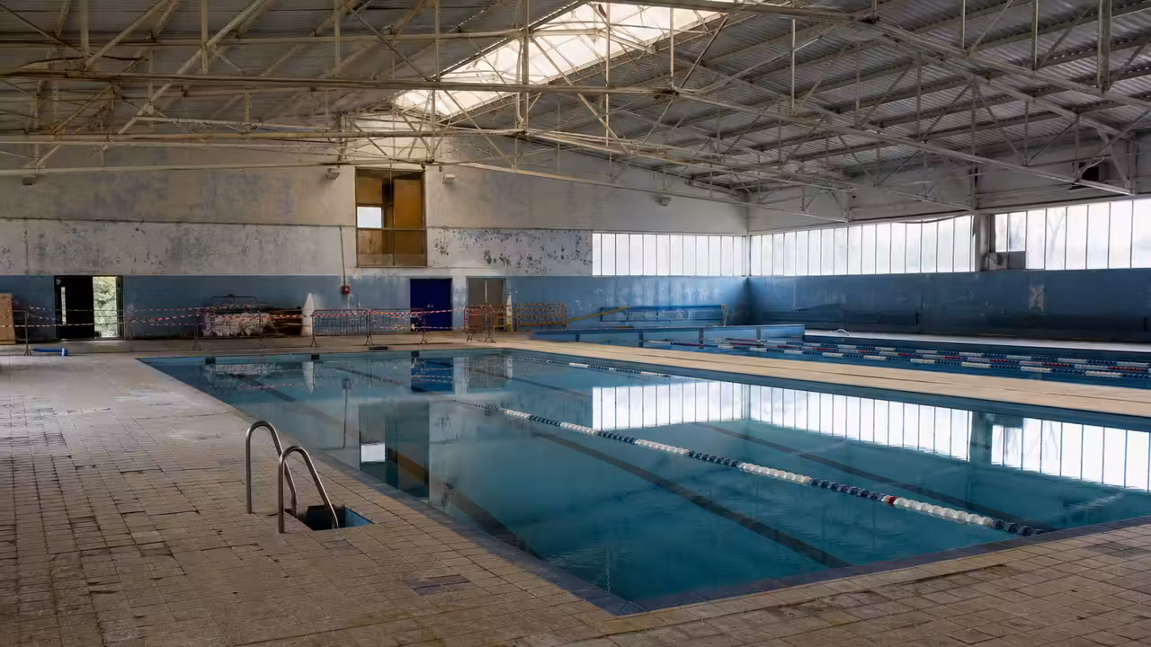 Bassin intérieur de piscine municipale fermé pour rénovation, avec échafaudage sous une charpente métallique
