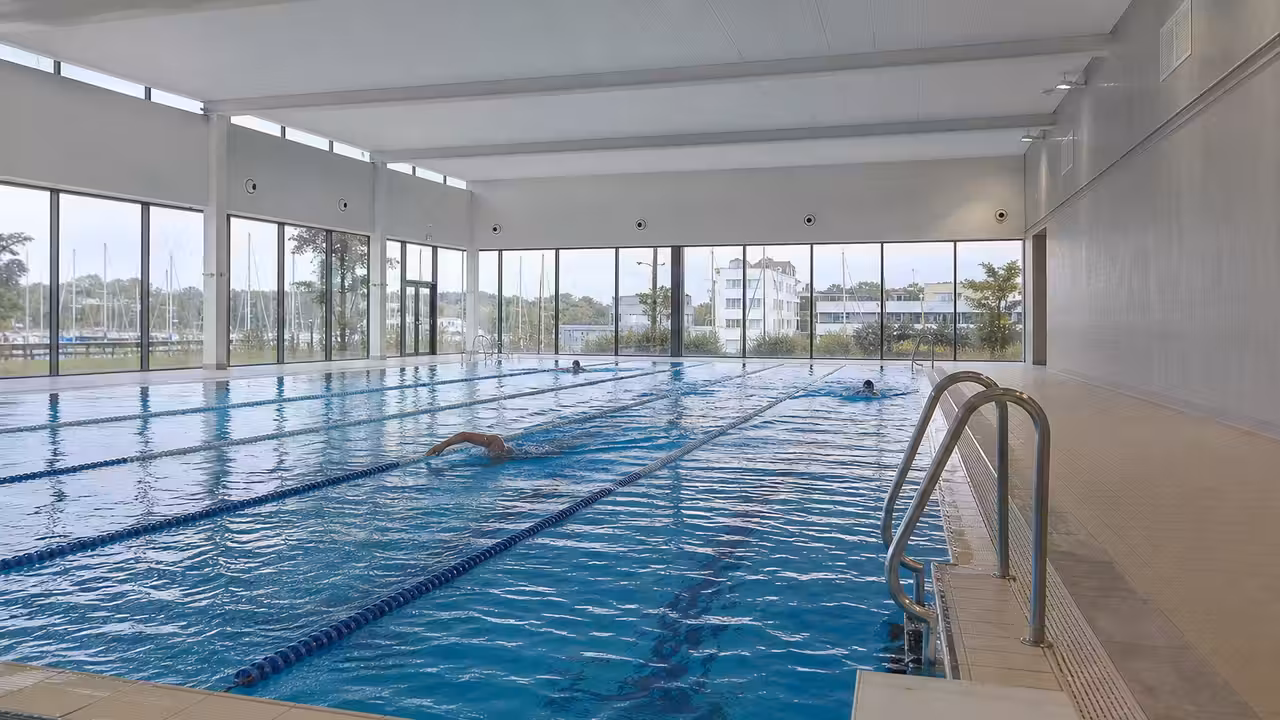 Bassin intérieur d’une piscine municipale rénovée, avec lignes de nage et larges baies vitrées