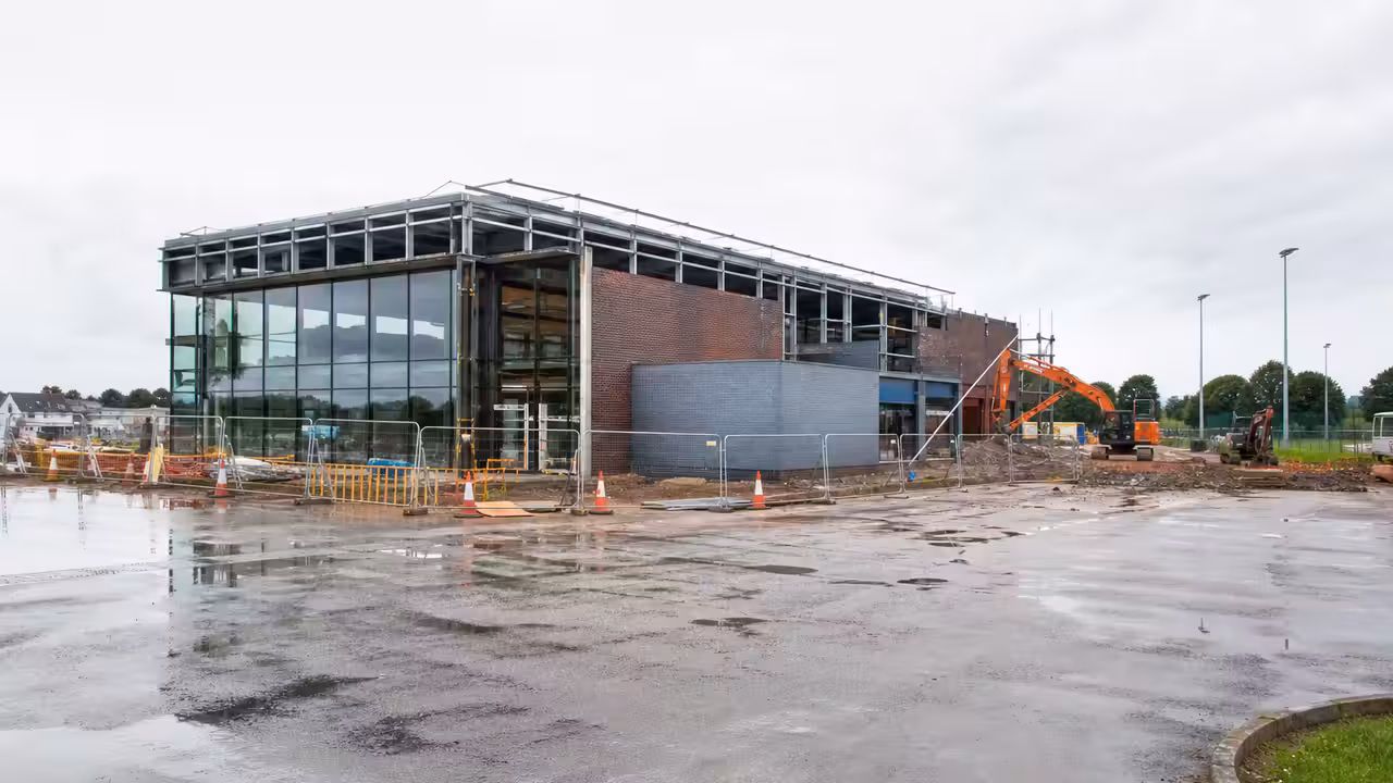 Chantier d’un centre aquatique avec structure de bâtiment, engins de travaux et aménagements sportifs en arrière-plan