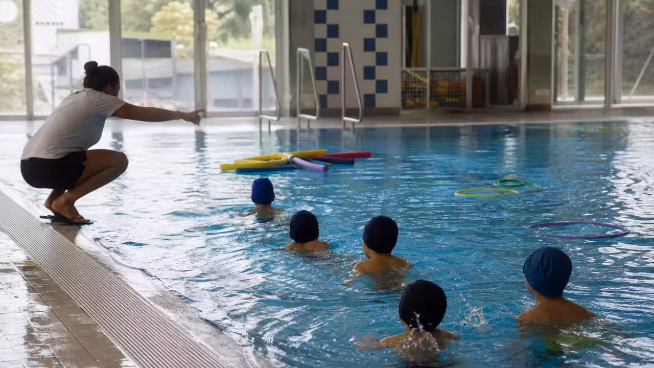 Élèves vus de dos participant à un atelier de natation encadré dans un bassin couvert municipal