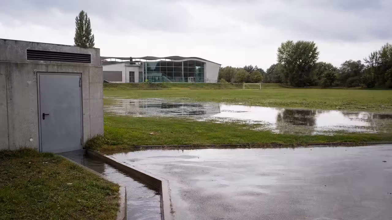 Terrain de sport détrempé après une forte pluie, avec flaques d’eau et système de drainage visible