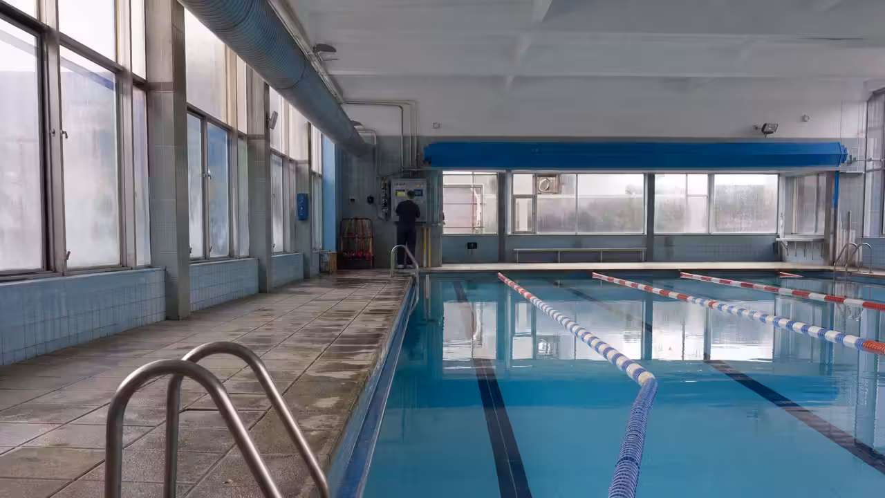 Bassin couvert municipal vide en début de journée, avec ventilation apparente et lignes d’eau calmes