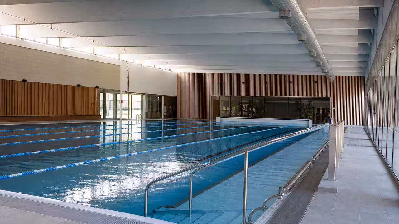Hall de bassin couvert rénové avec lignes d’eau, vestiaires vitrés et lumière naturelle diffuse
