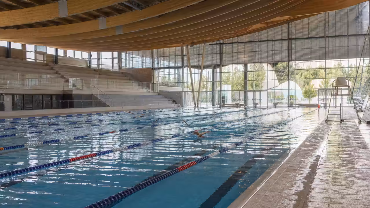 Nageurs dans les lignes d’un bassin couvert moderne de 50 mètres, avec tribunes et charpente en bois
