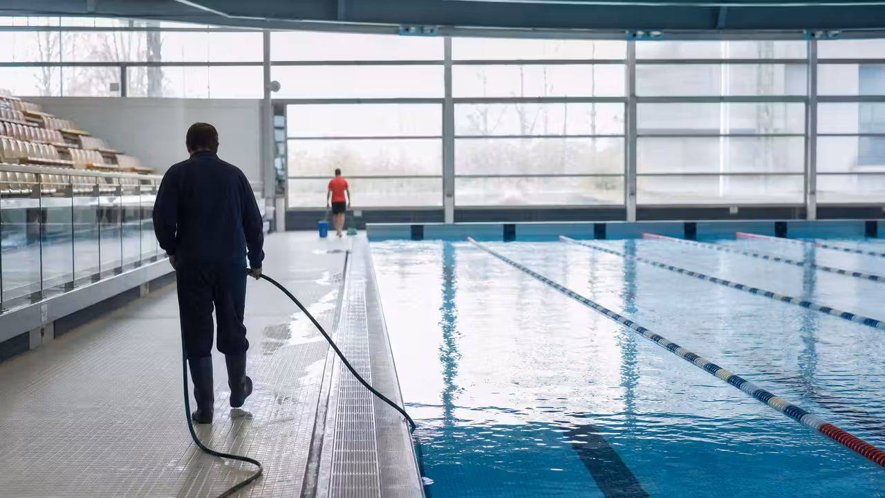 Bassin couvert de piscine publique avec lignes d’eau, gradins et personnel technique en arrière-plan