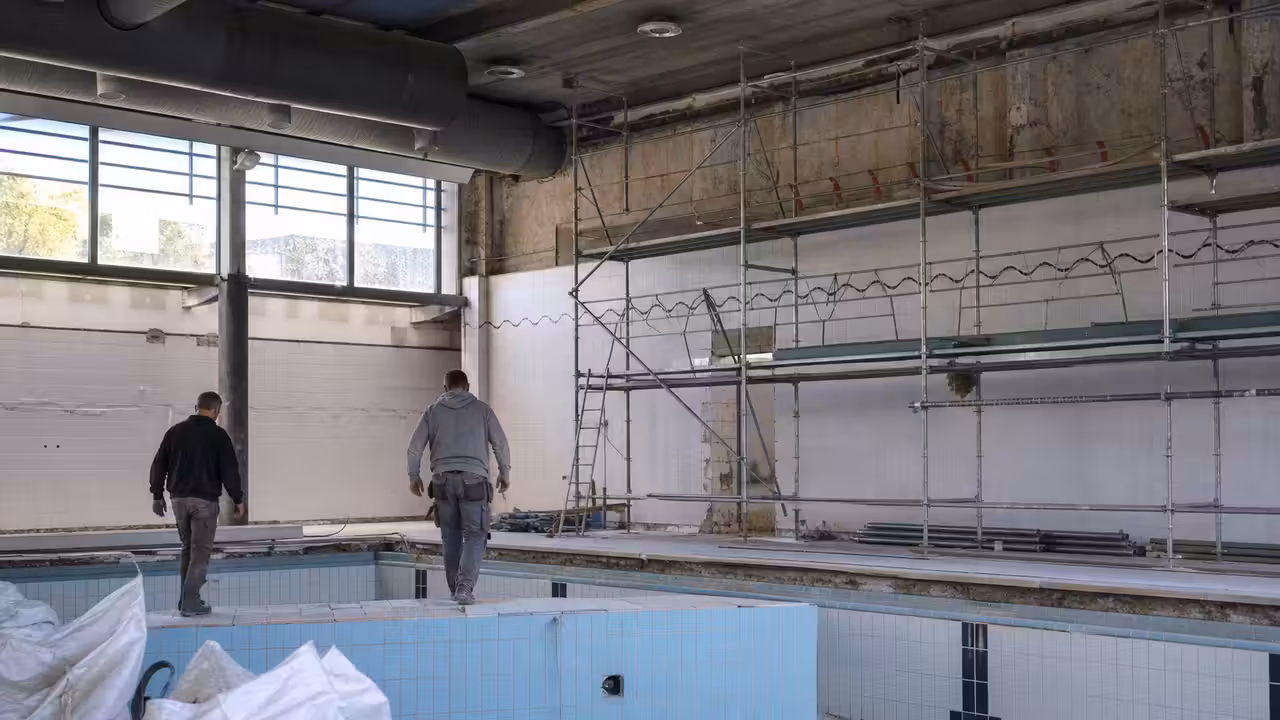 Bassin municipal couvert en rénovation, avec échafaudages et réseaux techniques visibles au bord de l’eau
