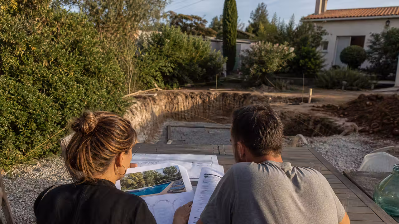 Couple examinant un plan et un devis près d’un terrain préparé pour une piscine enterrée
