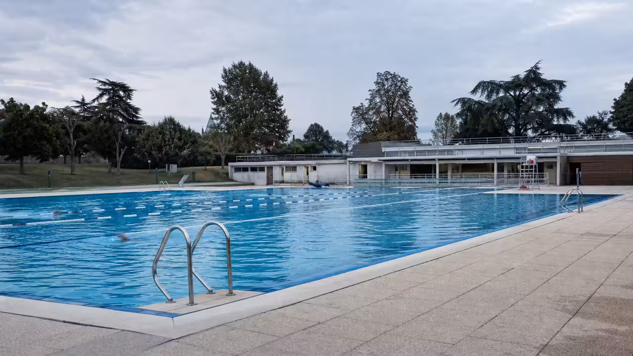 Bassin extérieur d’une piscine intercommunale avec nageurs et équipements techniques en arrière-plan