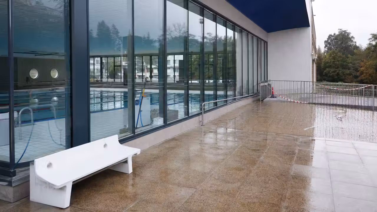 Bassin intérieur d’une piscine municipale vide, avec plages carrelées et panneaux de sécurité hors champ