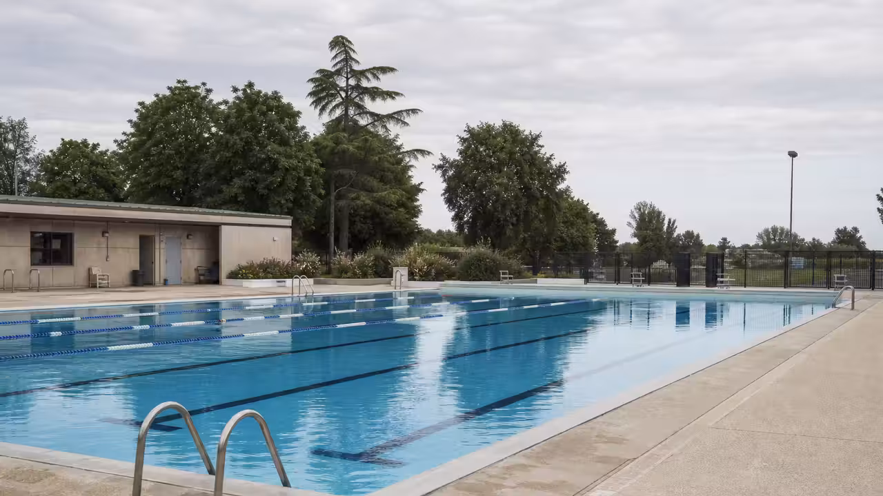 Bassin extérieur municipal vide en été, avec lignes d’eau et bâtiments techniques en arrière-plan
