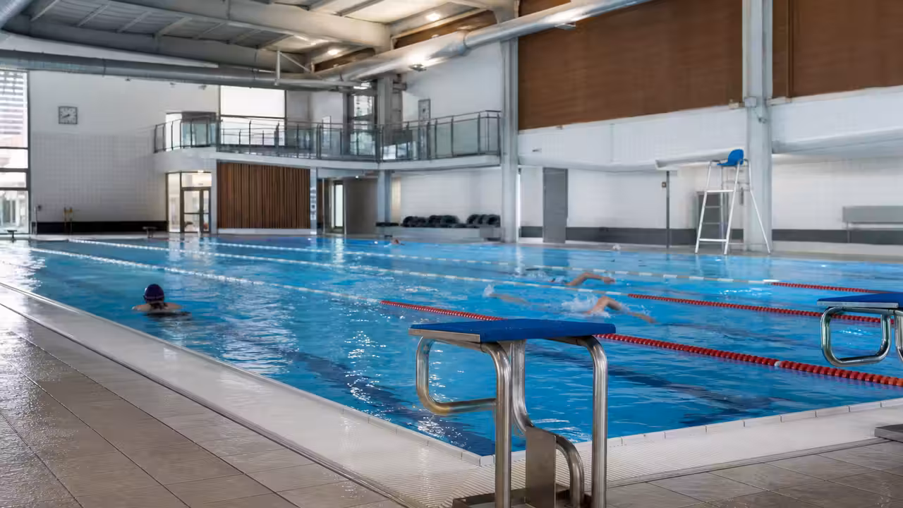 Bassin sportif intérieur de 25 mètres avec lignes d’eau, gradins et équipements techniques en arrière-plan
