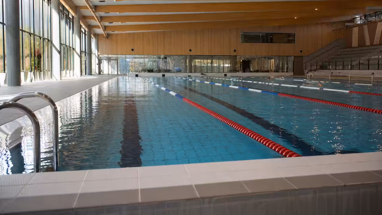 Bassin de natation couvert lumineux avec lignes d’eau, gradins discrets et architecture bois contemporaine
