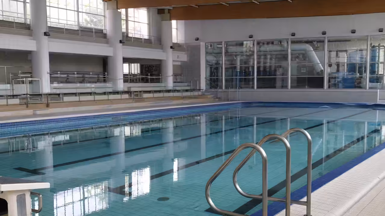 Bassin municipal vide avec lignes d’eau, gradins et équipements techniques en arrière-plan