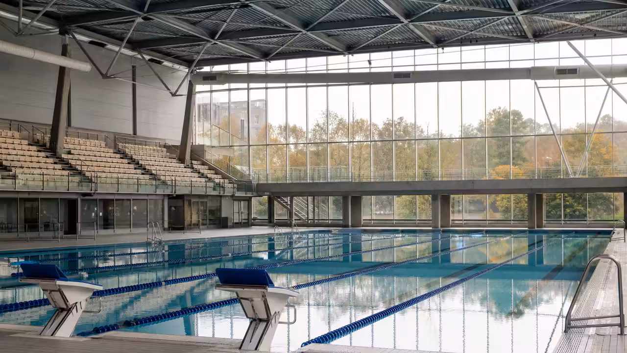 Bassin couvert moderne avec lignes d’eau, gradins latéraux et grande verrière dans un centre aquatique urbain