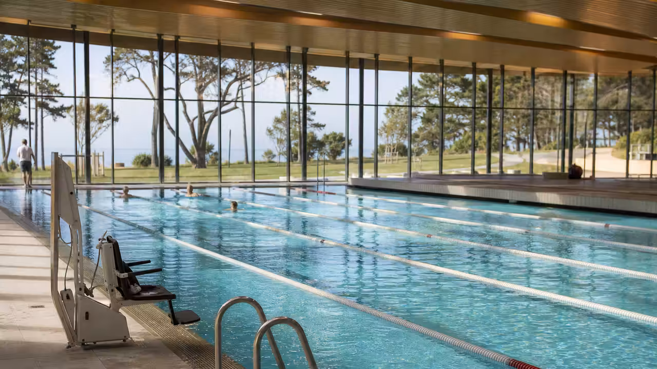 Piscine publique moderne à plusieurs couloirs intégrée dans un centre de sport et de bien-être paysager