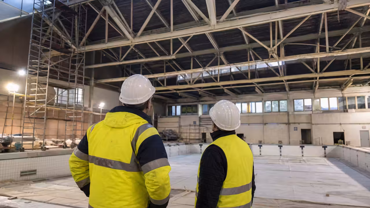 Techniciens inspectant la charpente et le plafond d’une piscine municipale vide en cours de rénovation