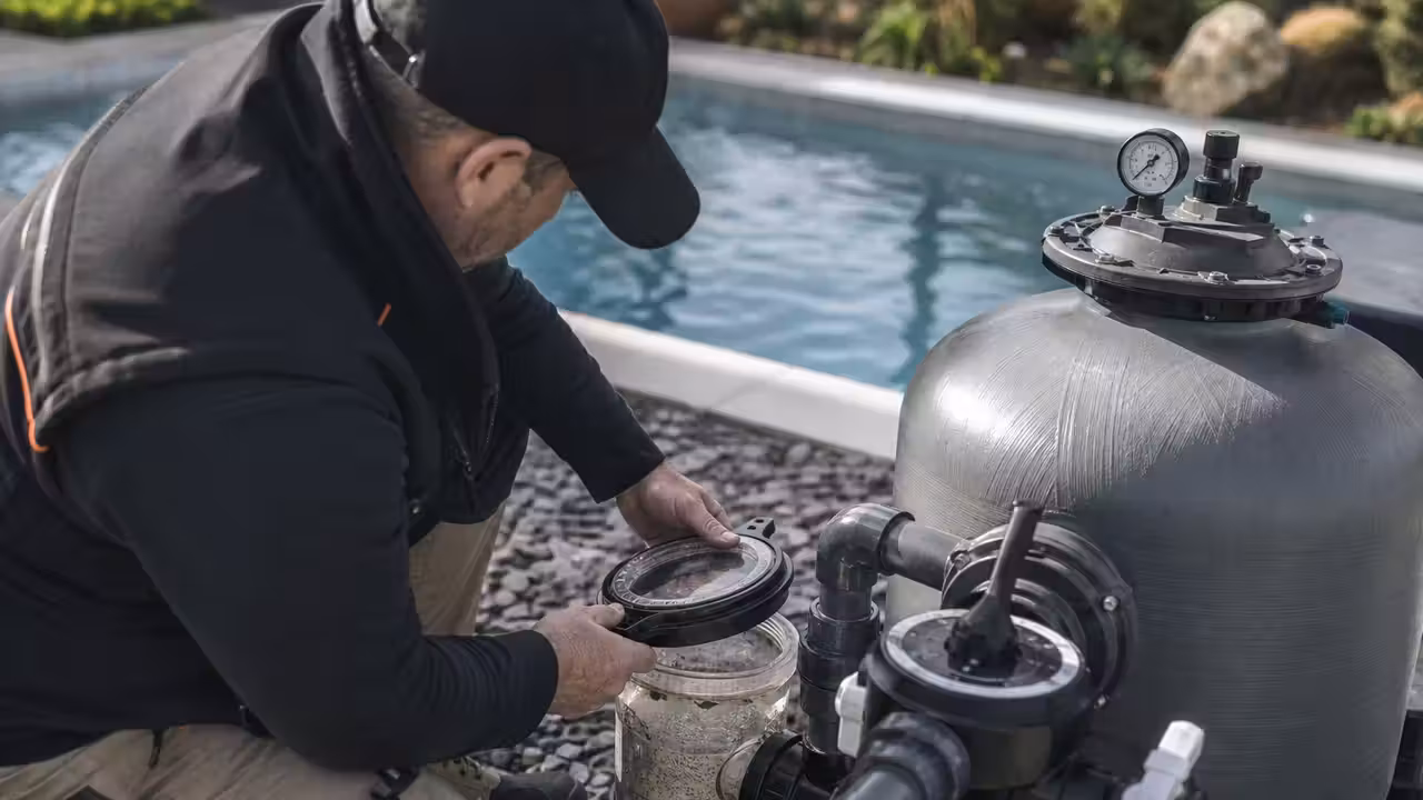 Technicien nettoyant le préfiltre d’une pompe devant une installation de filtration de piscine extérieure