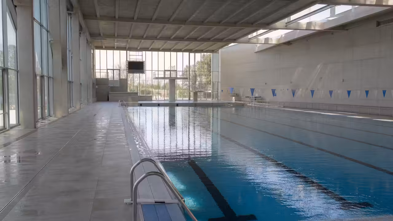 Bassin sportif couvert de 50 mètres avec lignes d’eau, gradins discrets et lumière naturelle latérale