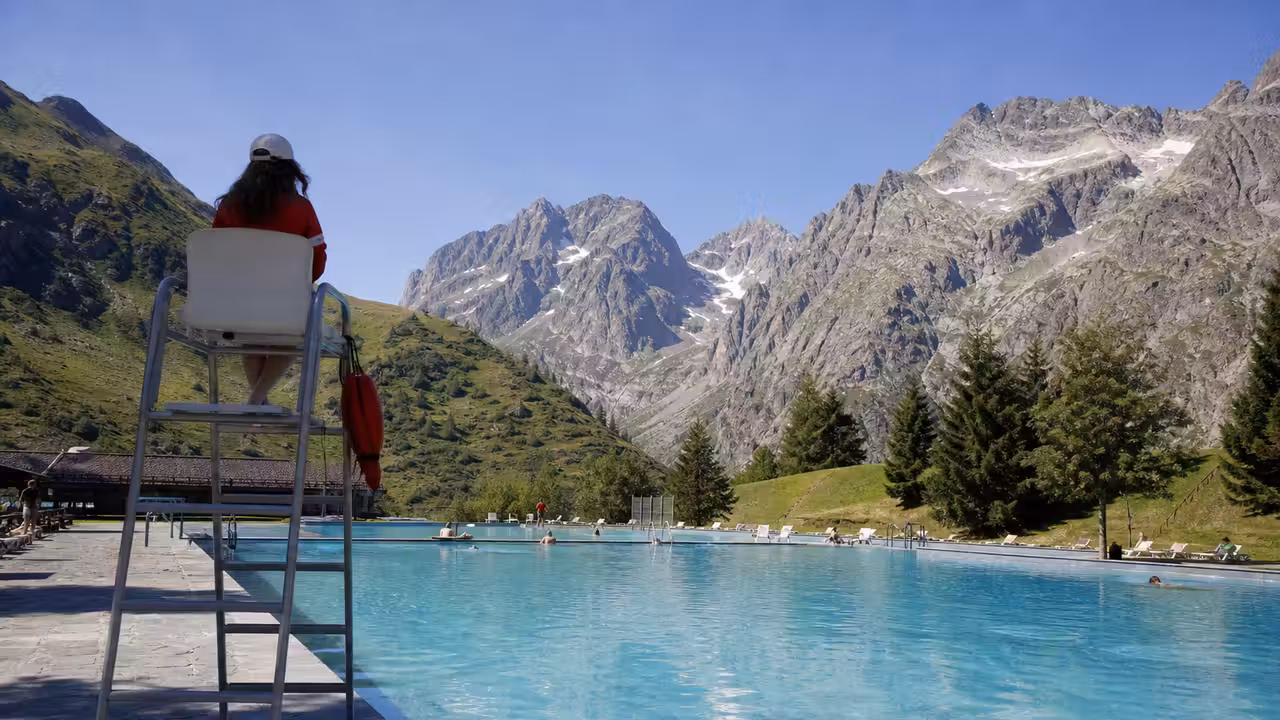 Baignade estivale dans un lac alpin, avec montagnes boisées et rive aménagée en arrière-plan