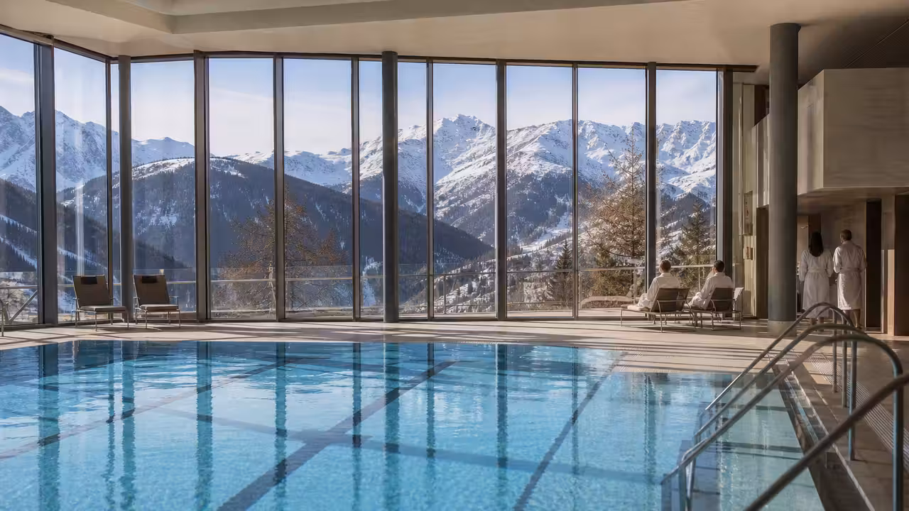 Bassin intérieur lumineux d’un complexe aquatique de montagne, avec baies vitrées sur des sommets enneigés