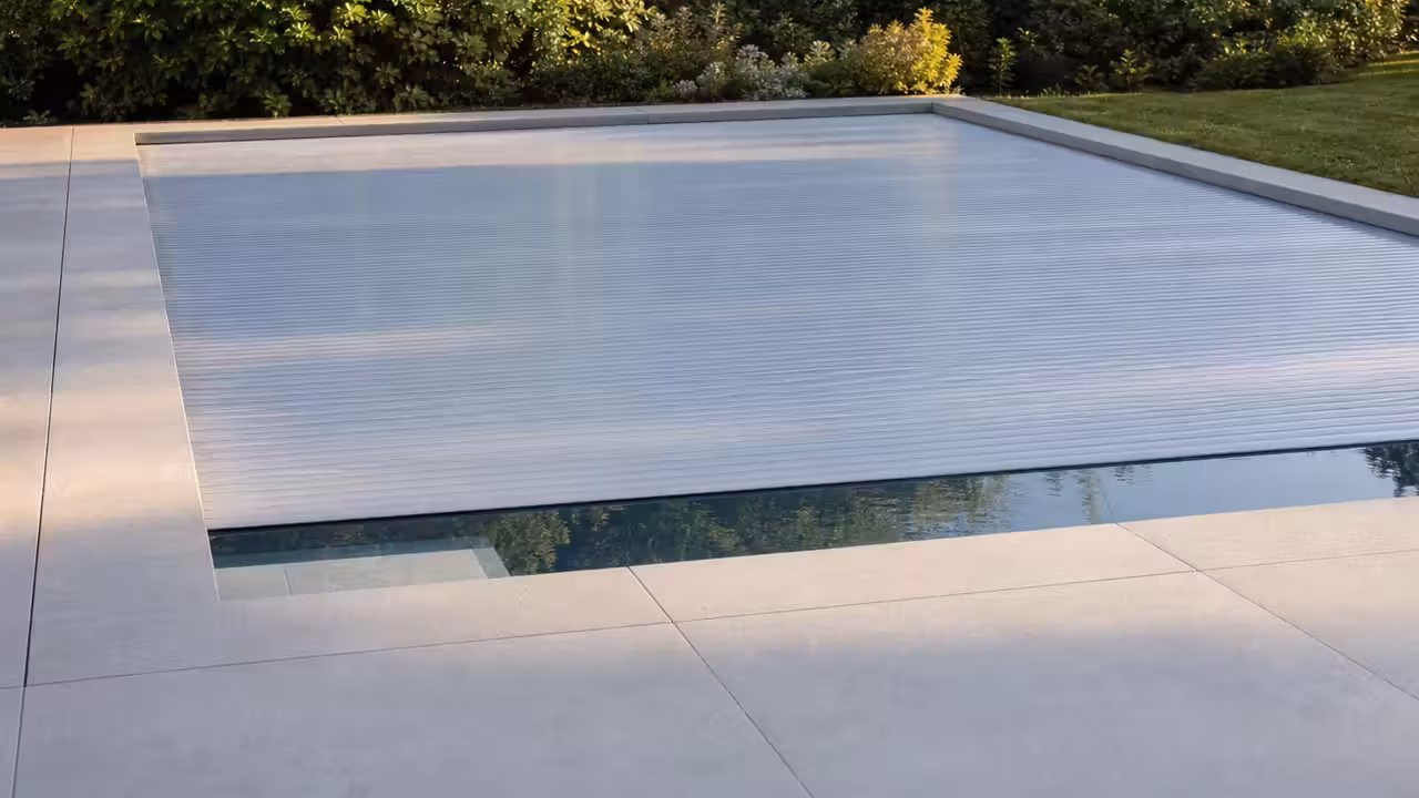 Volet roulant à lames fermé sur une piscine enterrée moderne, bordée de margelles claires