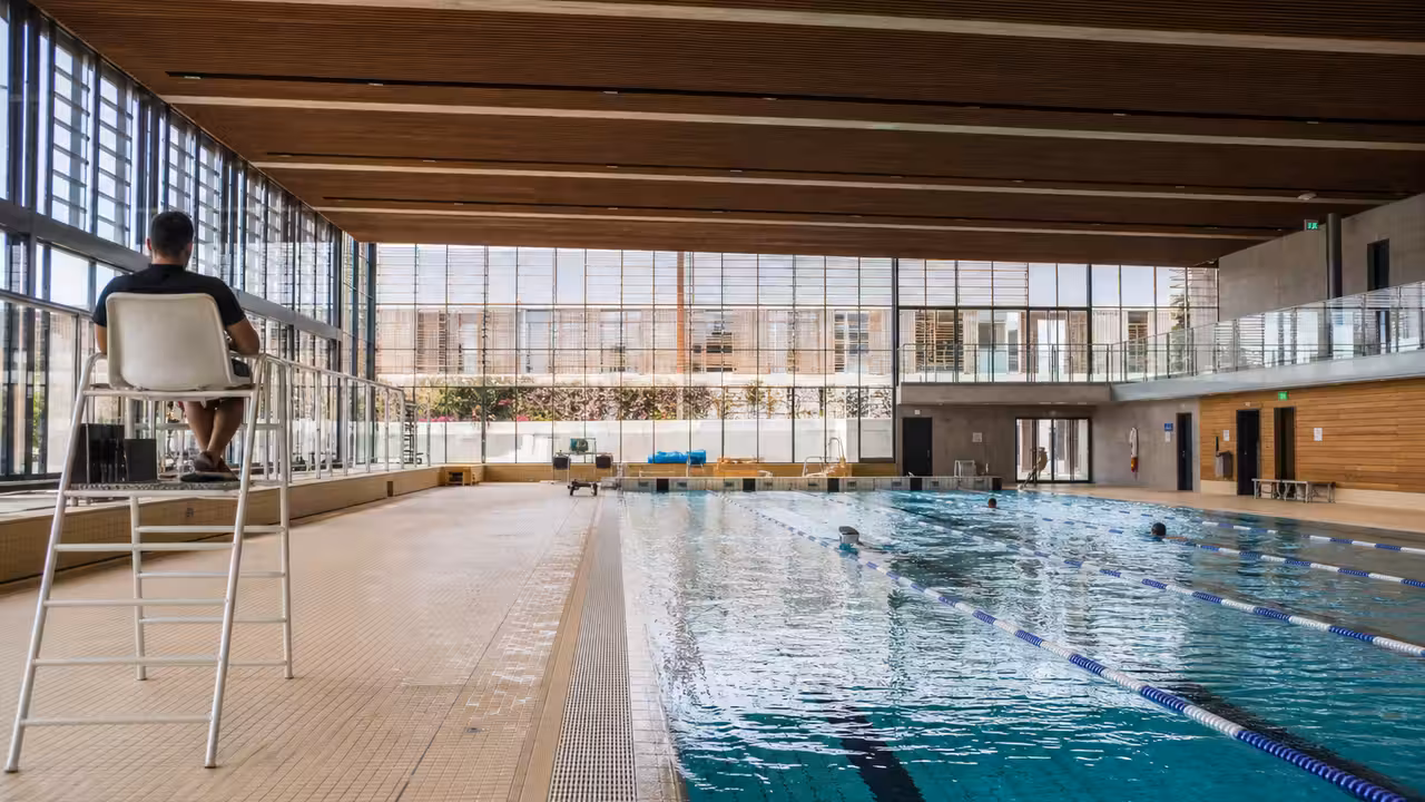 Bassin sportif rénové d’une piscine publique avec lignes d’eau, baigneurs au loin et baies vitrées