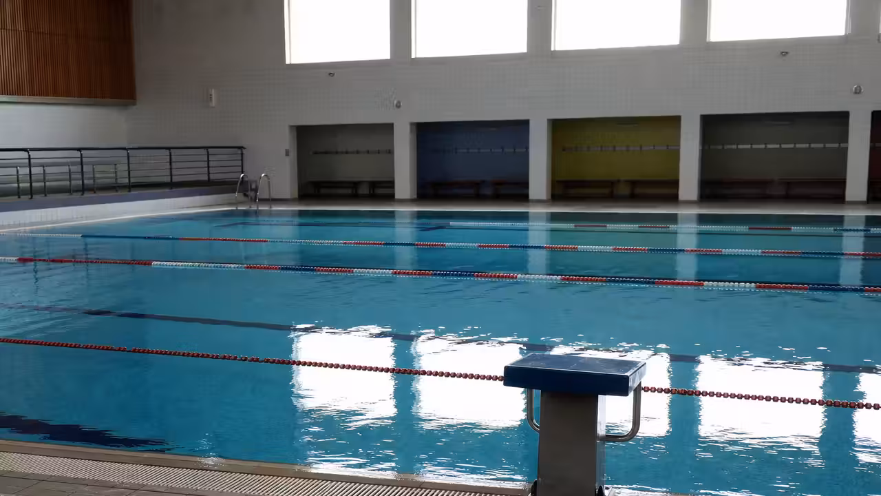 Bassin municipal vide avec lignes d’eau et plots de départ, éclairé par la lumière naturelle du matin