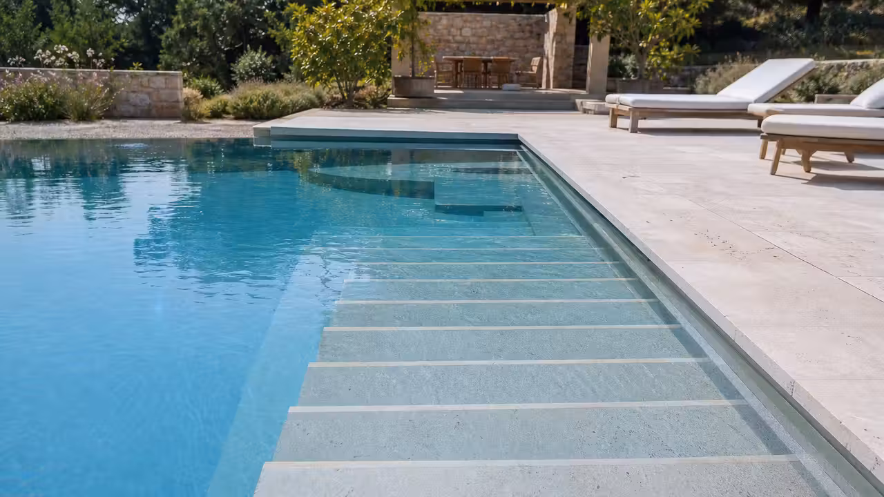 Escalier droit en larges marches dans une piscine contemporaine bordée d’une terrasse minérale claire