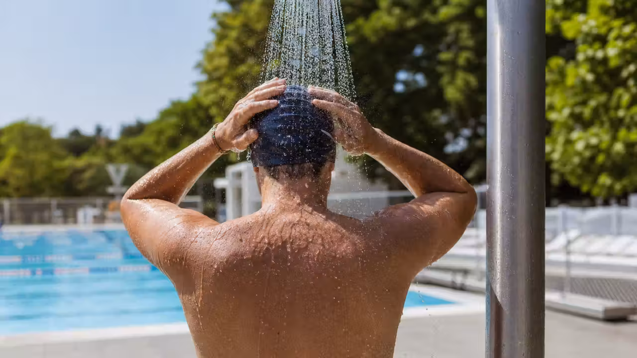 Baigneuse se rinçant sous une douche avant d’entrer dans une piscine collective lumineuse
