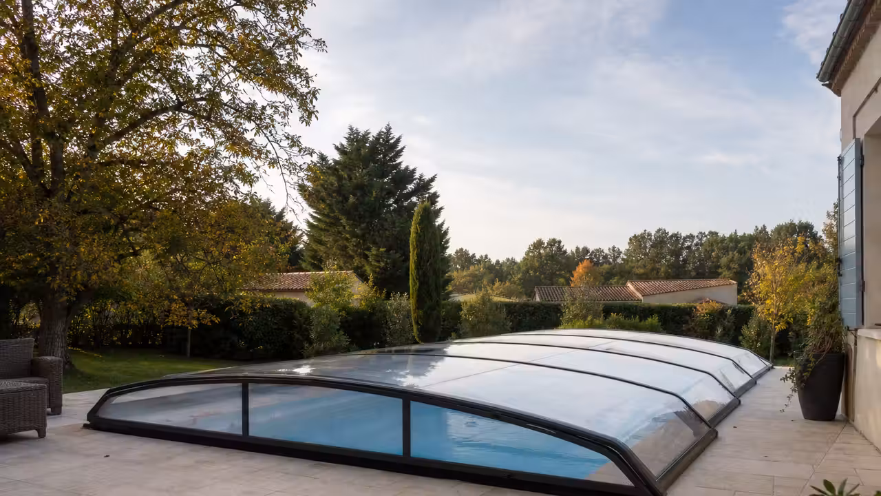 Abri télescopique bas fermé sur une piscine familiale, entouré d’une terrasse et d’un jardin arboré