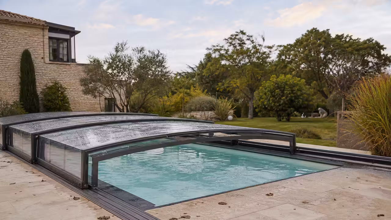 Abri télescopique bas en aluminium et panneaux transparents installé sur une piscine familiale avec terrasse