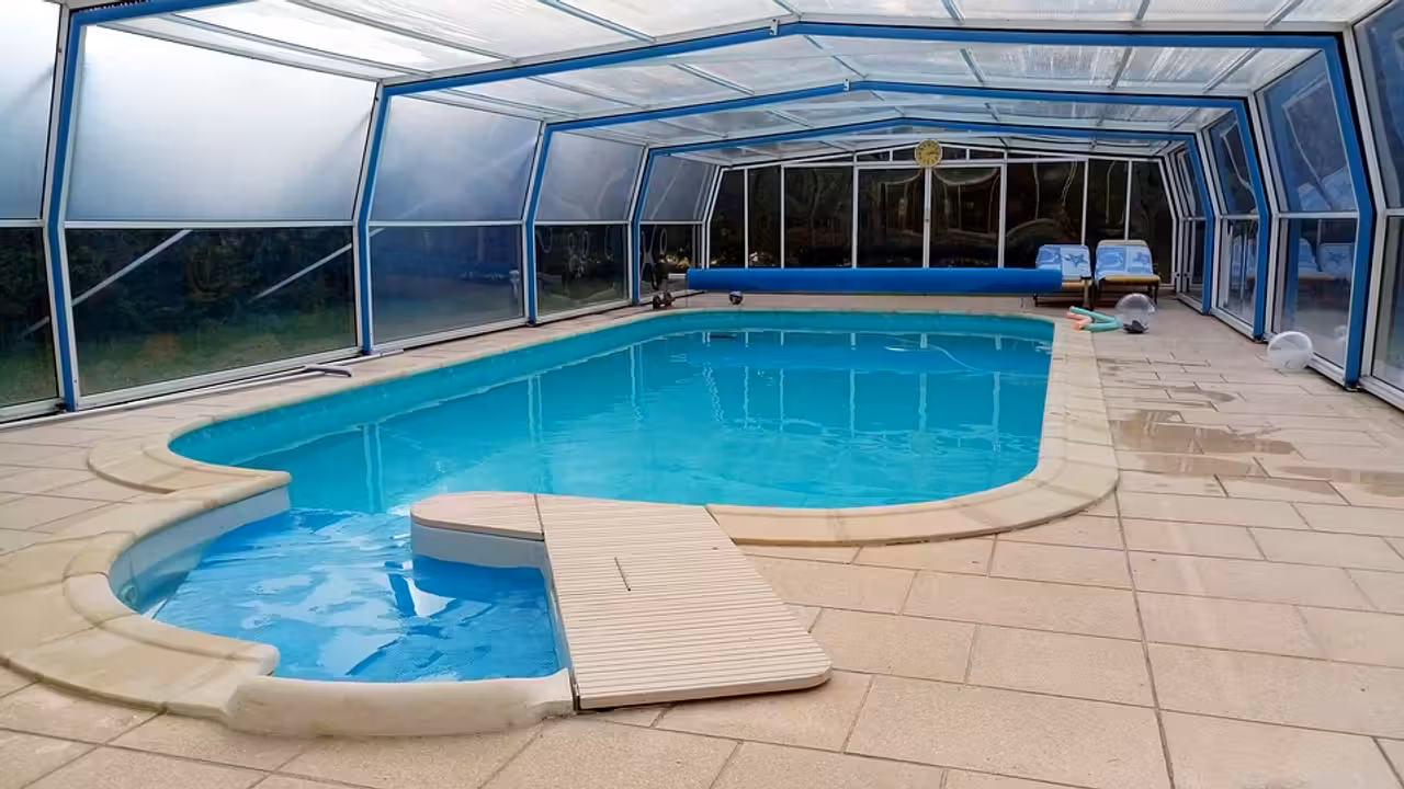 Abri télescopique bas en aluminium et polycarbonate couvrant une piscine rectangulaire dans un jardin arboré