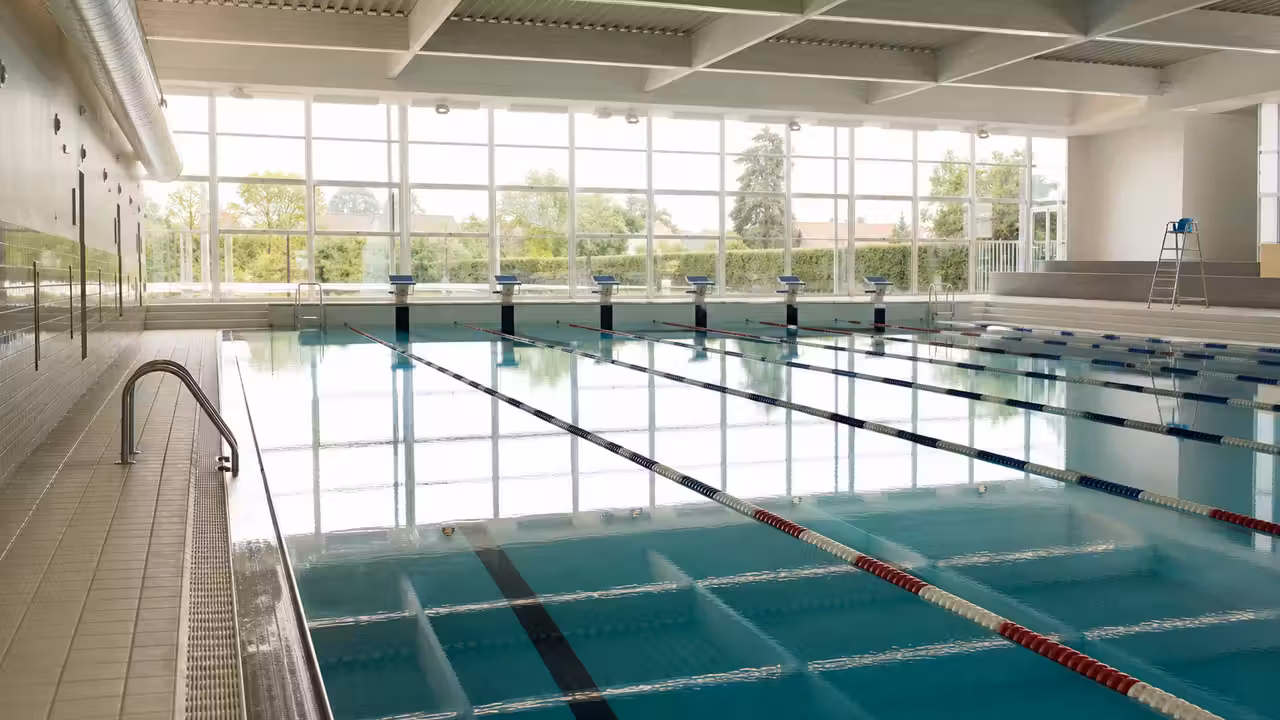 Bassin municipal couvert de 50 mètres avec lignes de nage et baies vitrées dans un équipement contemporain
