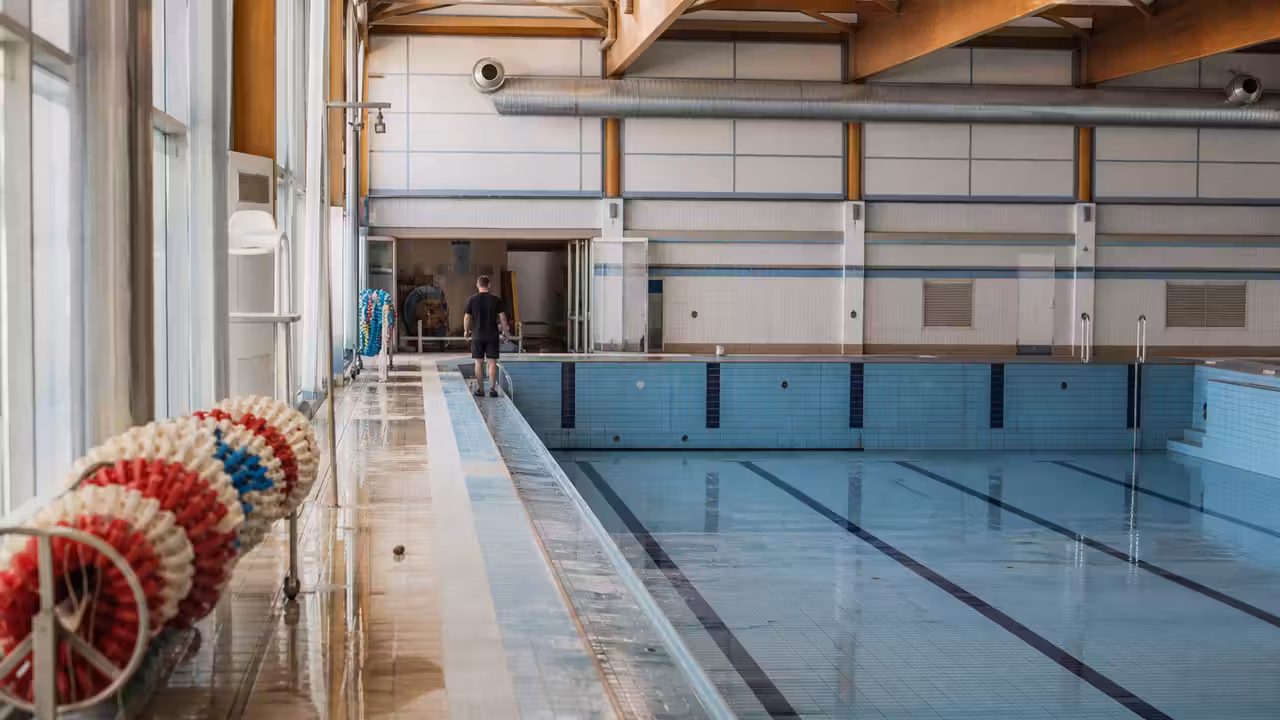 Bassin intérieur municipal vide pendant une opération de maintenance, avec lignes d’eau et locaux techniques en arrière-plan