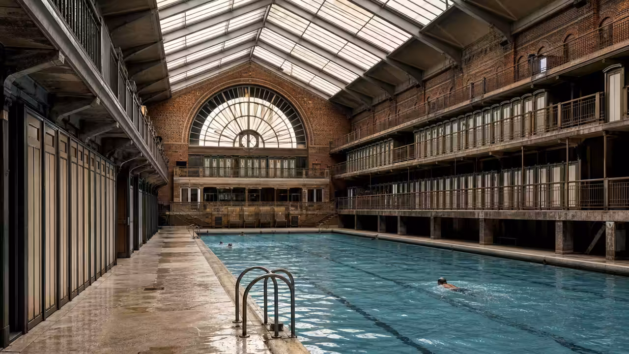 Vue intérieure d’une piscine parisienne historique avec verrière, bassin de nage et cabines en hauteur