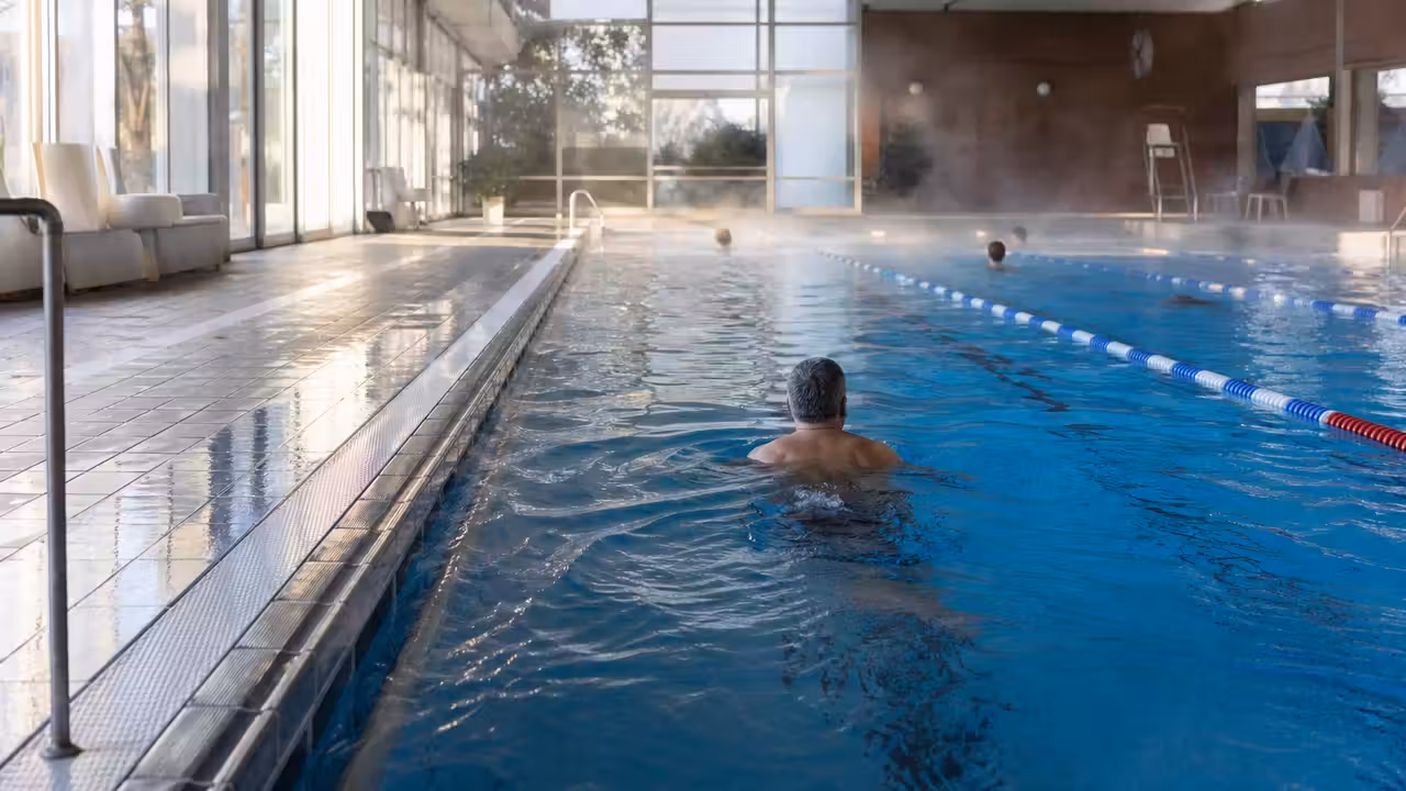 Bassin couvert de piscine publique avec lignes d’eau, vapeur légère et nageurs vus de dos