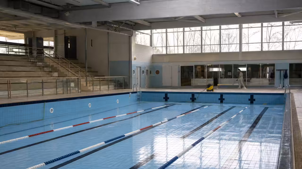Bassin intérieur municipal vide avec lignes d’eau, gradins et grandes baies vitrées à lumière naturelle