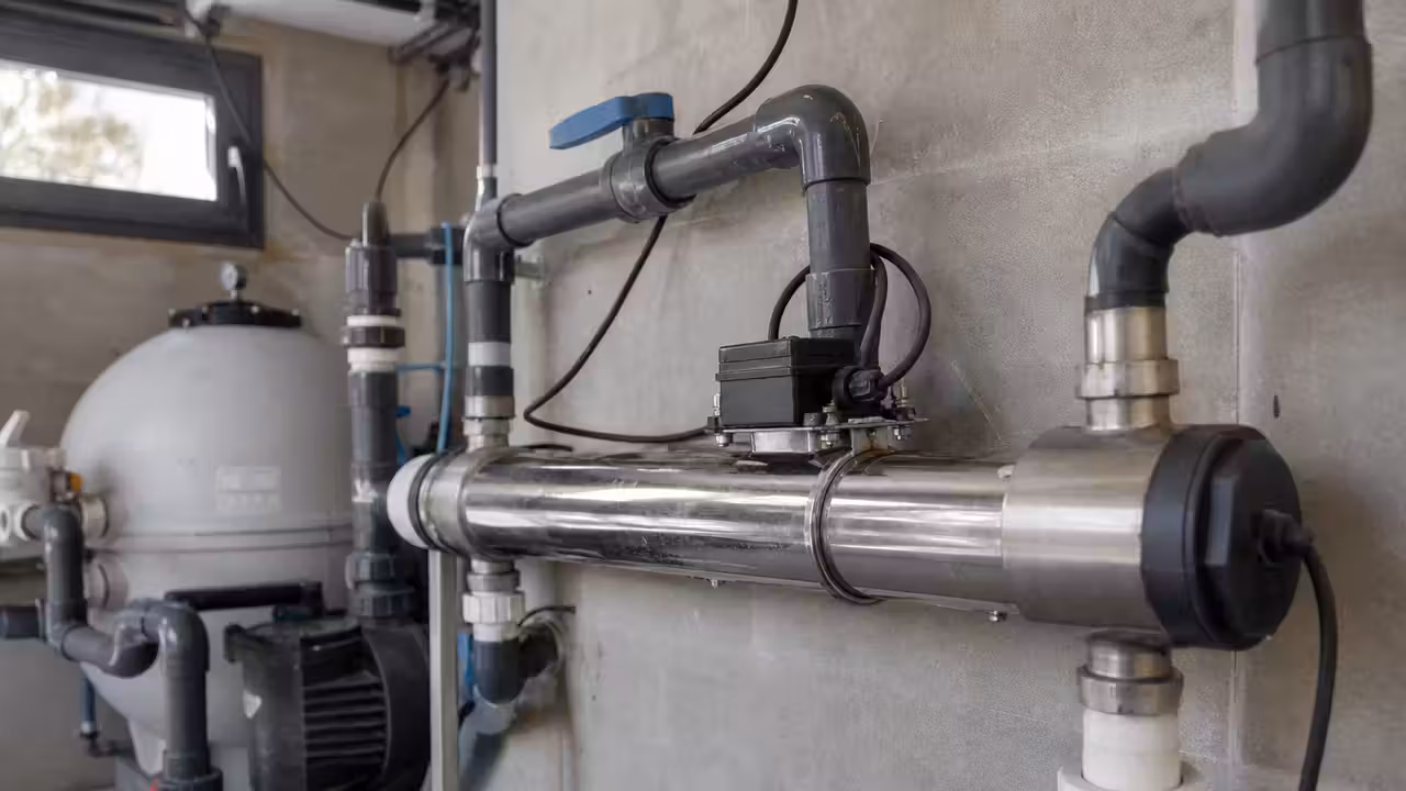 Réacteur UV en inox raccordé aux canalisations de filtration dans un local technique de piscine
