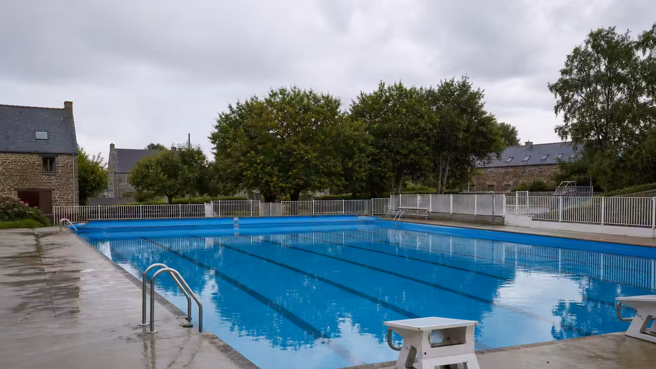 Bassin extérieur municipal vide au petit matin, bordé de végétation et prêt à accueillir les baigneurs