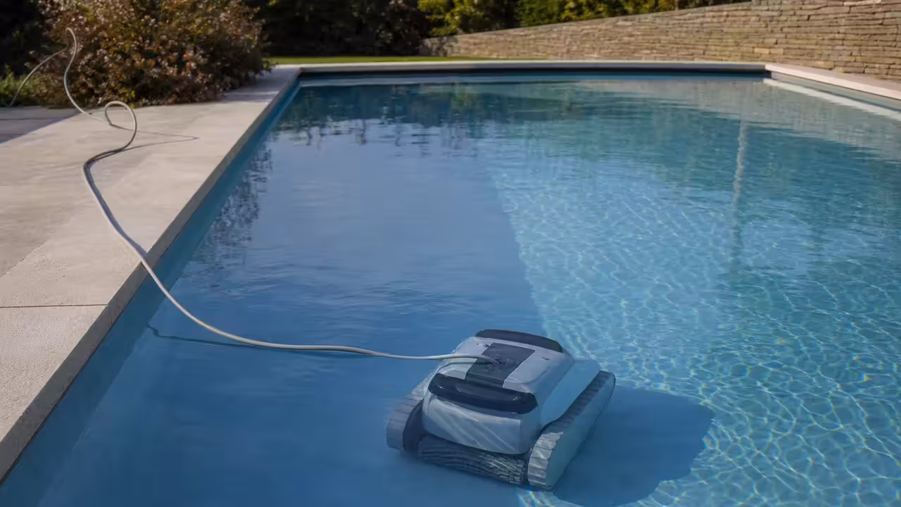 Robot électrique nettoyant le fond carrelé d’une piscine privée, avec son câble visible hors de l’eau