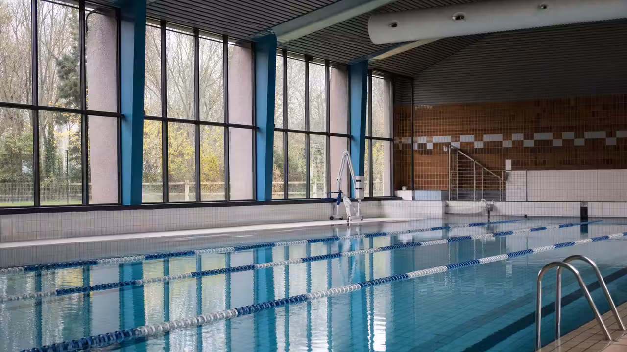 Vue intérieure d’une piscine municipale avec lignes d’eau, vestiaires en arrière-plan et lumière naturelle
