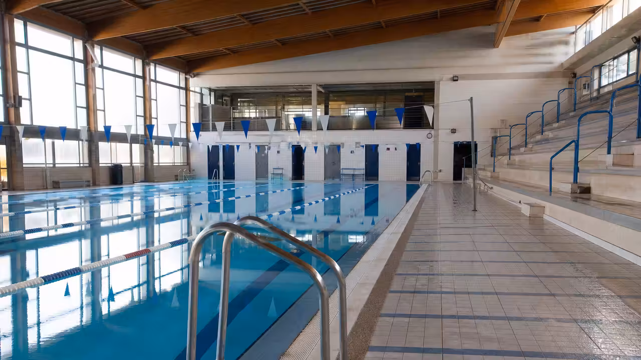 Bassin intérieur d’une piscine municipale avec lignes d’eau, gradins et lumière naturelle