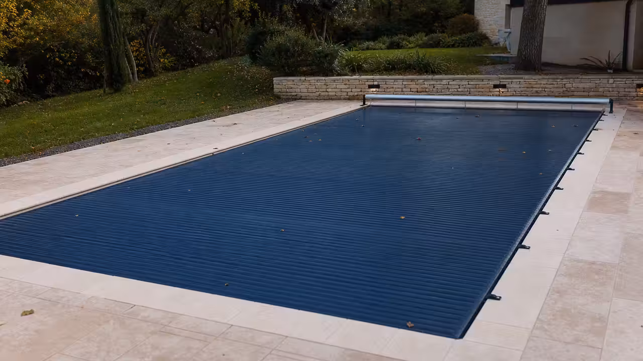 Bâche à barres tendue et verrouillée sur une piscine rectangulaire entourée de margelles en pierre