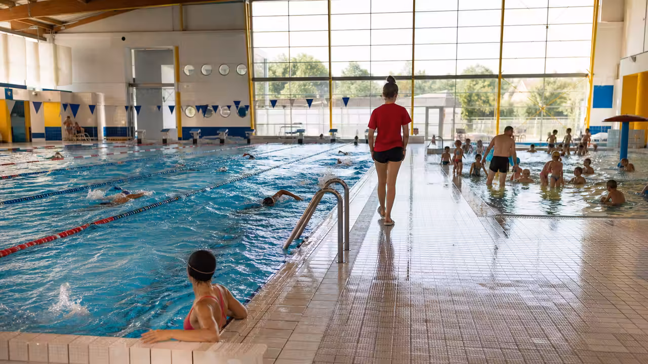 Nageurs et familles dans une piscine publique couverte durant une journée estivale très fréquentée