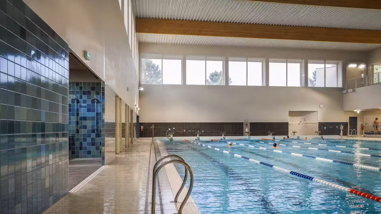 Intérieur lumineux d’une piscine municipale rénovée avec bassin, lignes d’eau, douches et vestiaires en arrière-plan